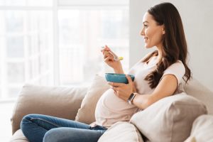 Smiling pregnant young woman having healthy breakfast